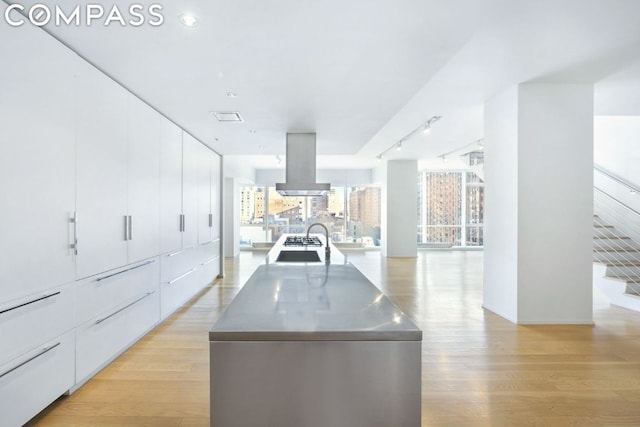 kitchen featuring light wood-style flooring, modern cabinets, stainless steel counters, and island range hood