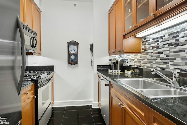 kitchen with stainless steel appliances, dark countertops, backsplash, a sink, and dark tile patterned floors