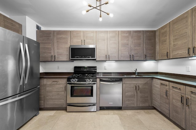 kitchen featuring stainless steel appliances, dark countertops, a notable chandelier, and a sink