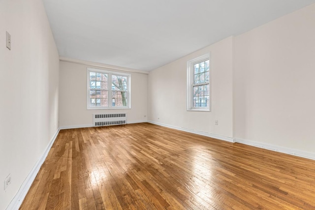 unfurnished room with radiator, a healthy amount of sunlight, and hardwood / wood-style flooring