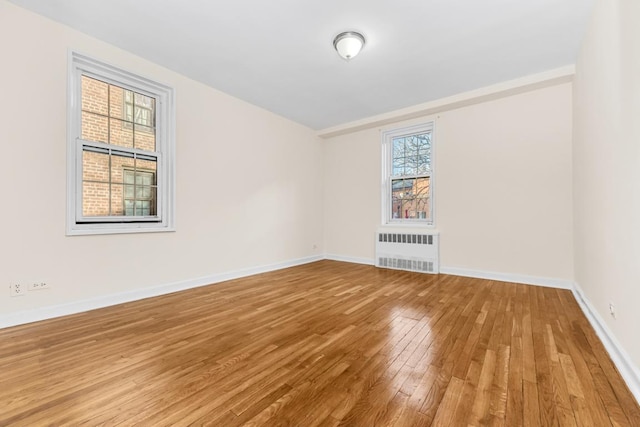 spare room with hardwood / wood-style floors, radiator heating unit, and a healthy amount of sunlight