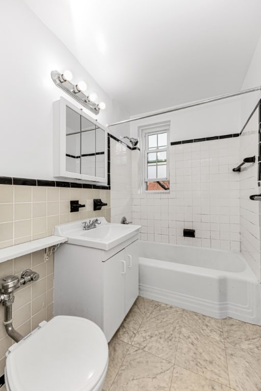 full bathroom with tile walls, toilet, vanity, and tiled shower / bath combo