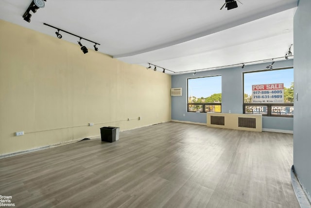 unfurnished living room with rail lighting, hardwood / wood-style floors, a wall unit AC, and a wealth of natural light