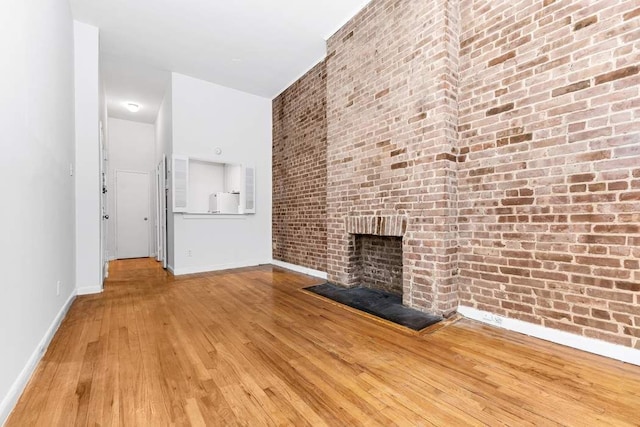 unfurnished living room featuring a brick fireplace, brick wall, and hardwood / wood-style flooring