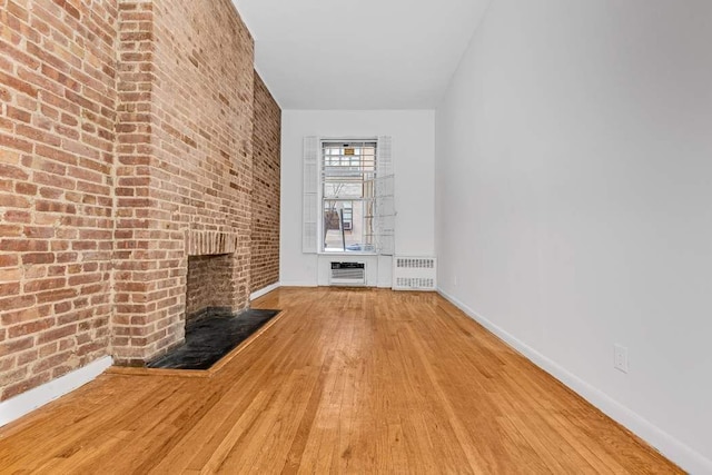 unfurnished living room featuring a brick fireplace, brick wall, radiator heating unit, and hardwood / wood-style flooring