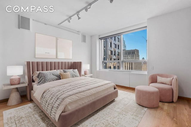 bedroom with a city view, track lighting, visible vents, and wood finished floors