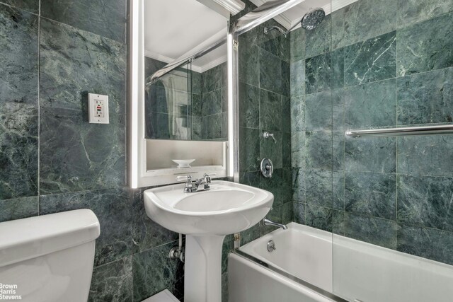 bathroom featuring bath / shower combo with glass door, tile walls, crown molding, and toilet