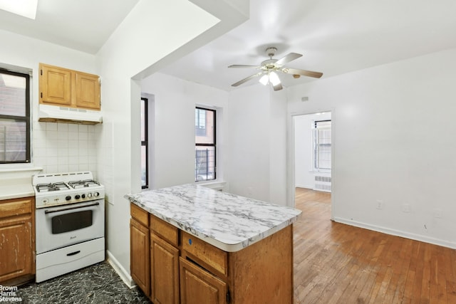 kitchen with white range with gas stovetop, decorative backsplash, light countertops, radiator, and under cabinet range hood