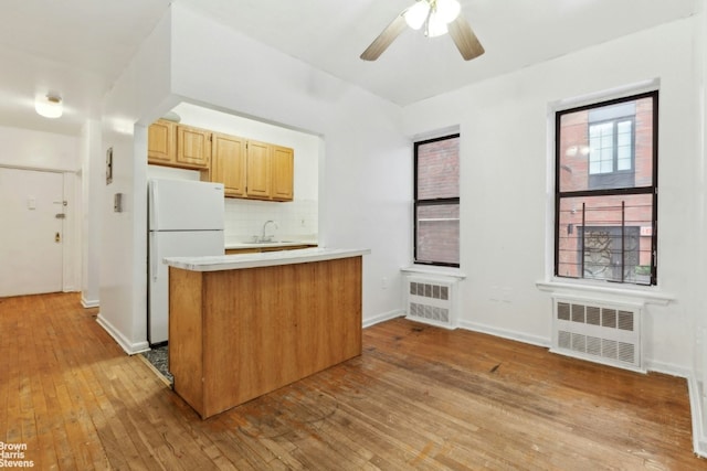 kitchen featuring tasteful backsplash, light countertops, radiator heating unit, freestanding refrigerator, and a sink