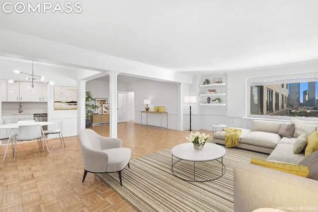 living room featuring ornate columns, light parquet floors, built in features, a chandelier, and crown molding