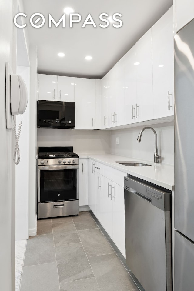 kitchen with stainless steel appliances, a sink, white cabinets, light countertops, and modern cabinets