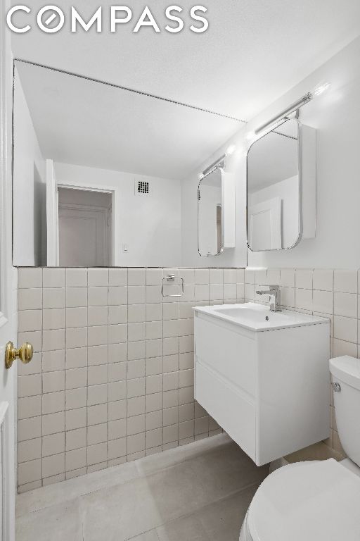 bathroom featuring toilet, vanity, and tile walls