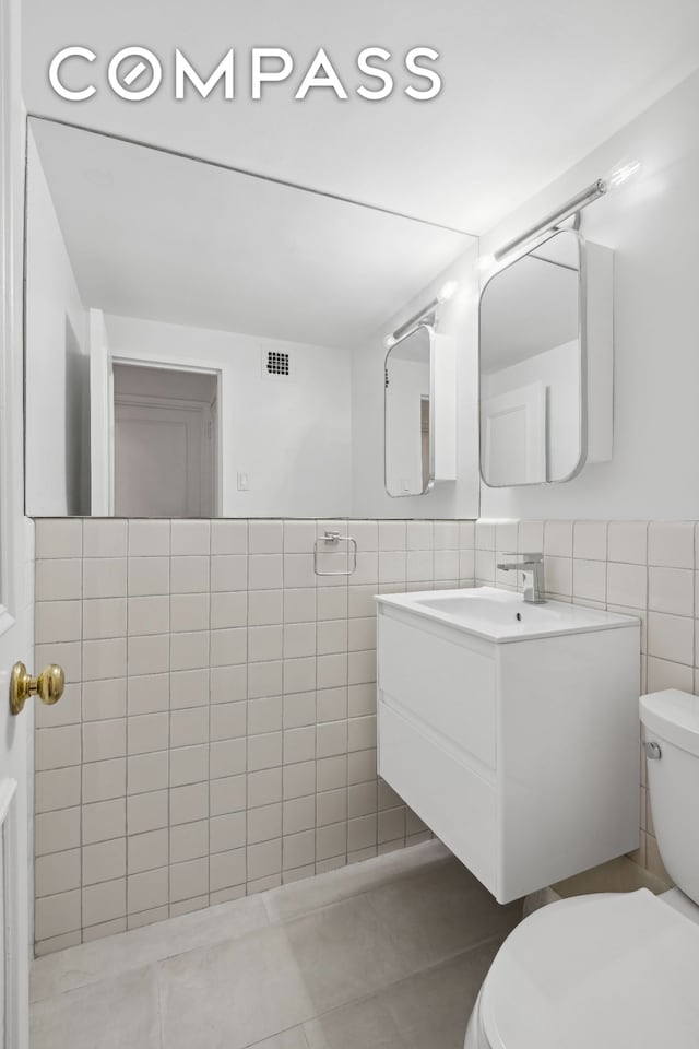 half bathroom featuring toilet, visible vents, vanity, tile walls, and wainscoting