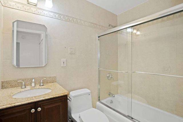 full bathroom with shower / bath combination with glass door, vanity, toilet, and tile walls