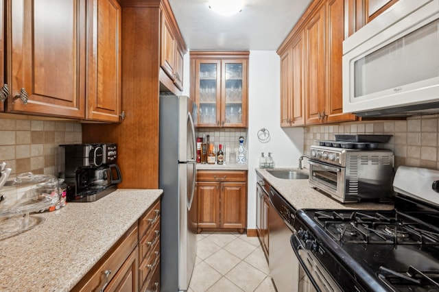 kitchen featuring sink, light stone counters, light tile patterned floors, appliances with stainless steel finishes, and backsplash