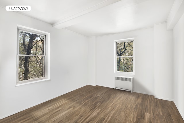 empty room featuring visible vents, plenty of natural light, dark wood-type flooring, and radiator heating unit