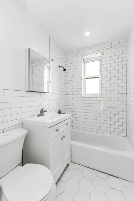 full bathroom with tiled shower / bath combo, tile patterned flooring, vanity, tile walls, and toilet