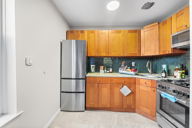 kitchen with light stone counters, sink, backsplash, and appliances with stainless steel finishes