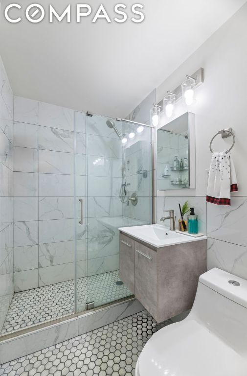 bathroom with a shower with shower door, tile walls, toilet, and vanity