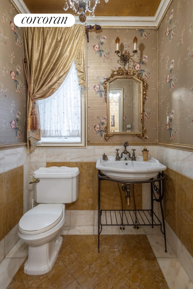 half bathroom featuring toilet, wallpapered walls, a sink, and wainscoting