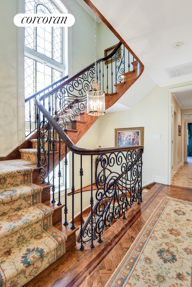 staircase featuring high vaulted ceiling, wood finished floors, visible vents, baseboards, and crown molding