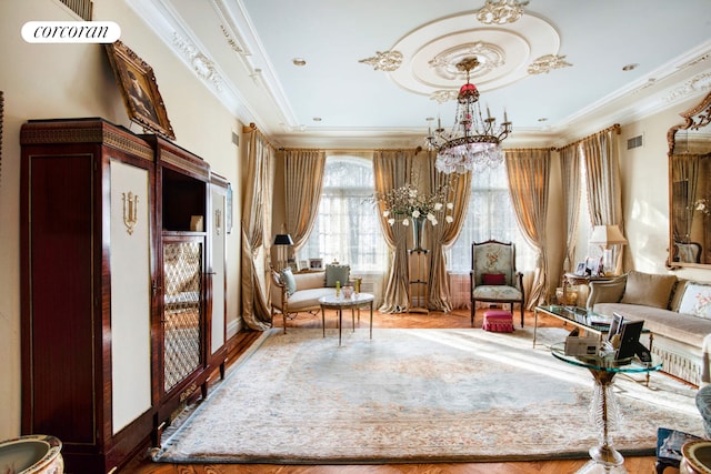 living area featuring an inviting chandelier, visible vents, wood finished floors, and ornamental molding