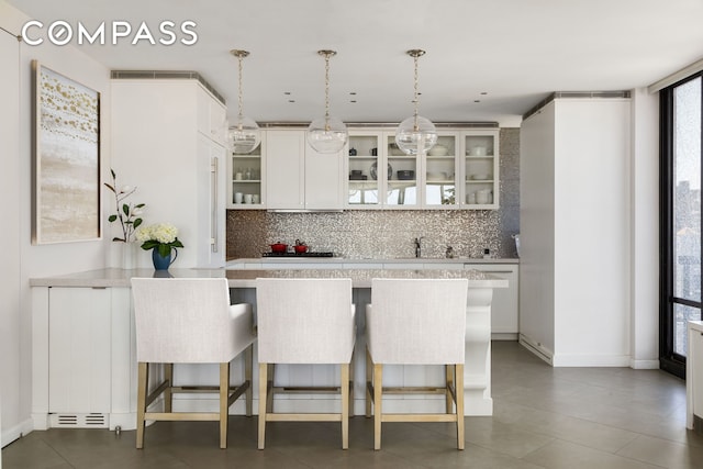 kitchen featuring glass insert cabinets, a breakfast bar, light countertops, and backsplash