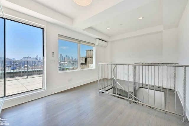 unfurnished room with a raised ceiling, wood-type flooring, a healthy amount of sunlight, and a wall mounted AC