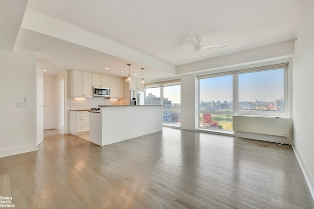 interior space with tasteful backsplash, white cabinets, hanging light fixtures, stainless steel appliances, and light wood-style floors