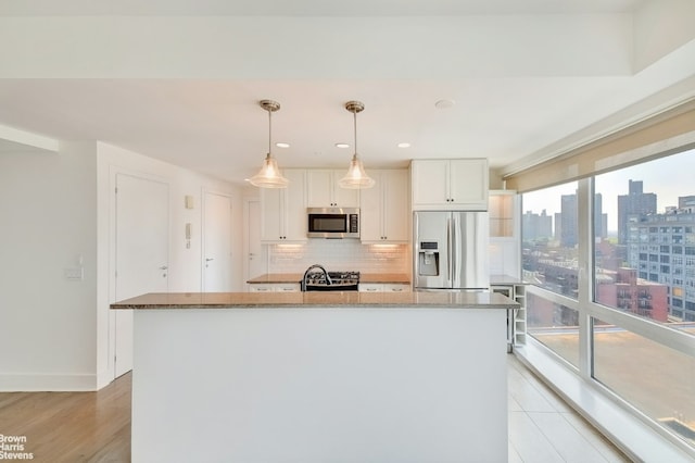 kitchen with stone counters, stainless steel appliances, white cabinets, and an island with sink