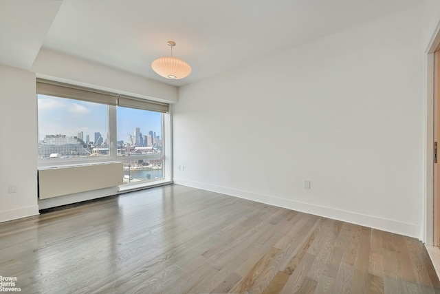 unfurnished room with a view of city, baseboards, and wood finished floors