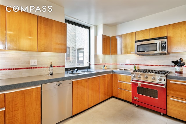 kitchen with stainless steel appliances, dark countertops, brown cabinetry, and a sink