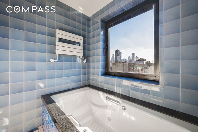 bathroom with a view of city, radiator heating unit, tile walls, and a whirlpool tub