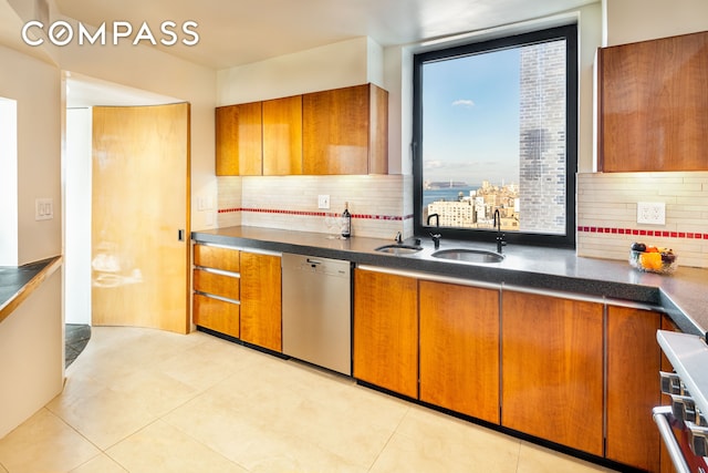 kitchen featuring stainless steel dishwasher, dark countertops, a sink, and brown cabinets