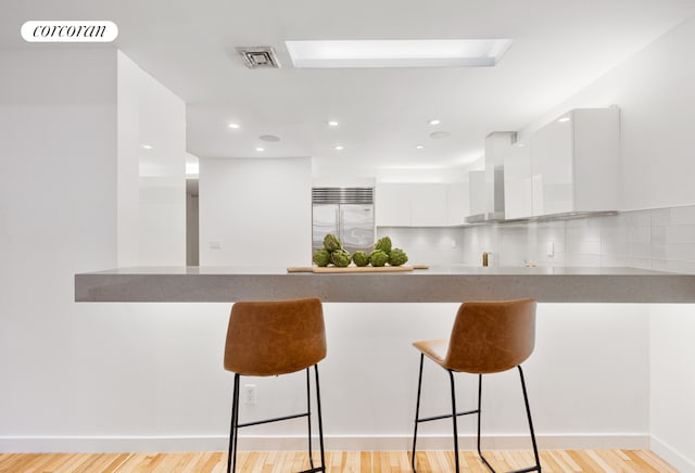 kitchen featuring white cabinets, wall chimney exhaust hood, modern cabinets, built in refrigerator, and a peninsula