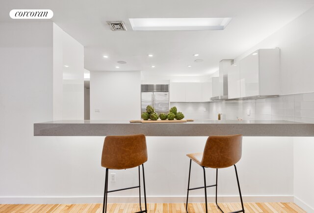 176 Broadway Unit 3C, New York City, NY 10038 - kitchen with stainless steel built in refrigerator, a peninsula, wall chimney exhaust hood, modern cabinets, and white cabinets