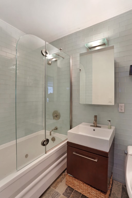 full bathroom with tile walls, vanity, bath / shower combo with glass door, and toilet