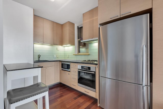 kitchen featuring dark countertops, dark wood-type flooring, under cabinet range hood, tasteful backsplash, and stainless steel appliances