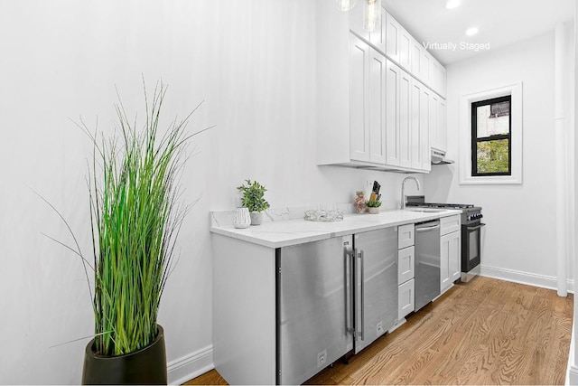 kitchen with sink, appliances with stainless steel finishes, white cabinetry, light stone countertops, and light hardwood / wood-style floors