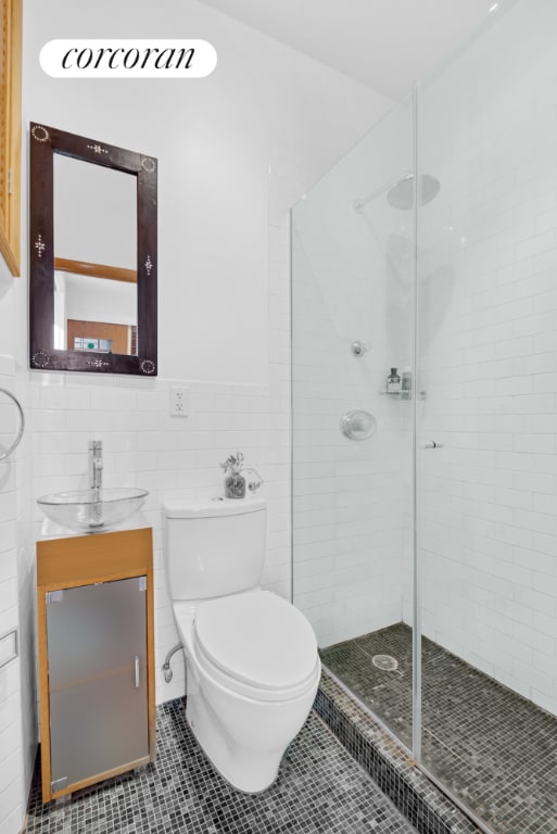 bathroom featuring toilet, walk in shower, tile walls, tile patterned floors, and sink