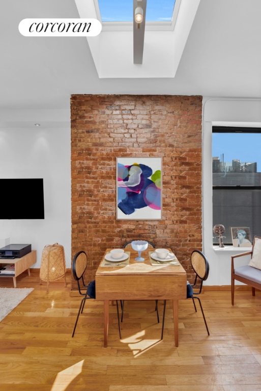 dining room featuring brick wall, a skylight, and wood finished floors