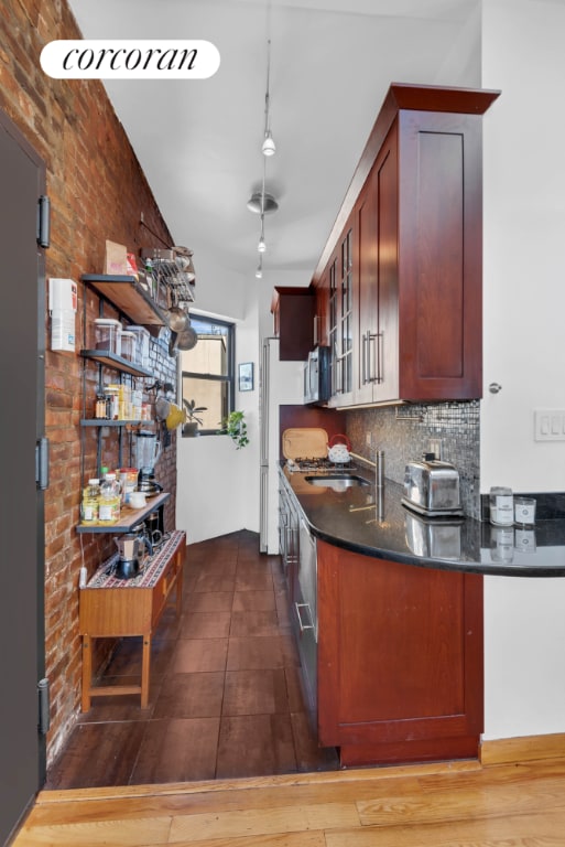 kitchen featuring a sink, decorative backsplash, stainless steel microwave, dark countertops, and glass insert cabinets