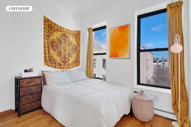 bedroom with light wood finished floors, a baseboard radiator, and visible vents