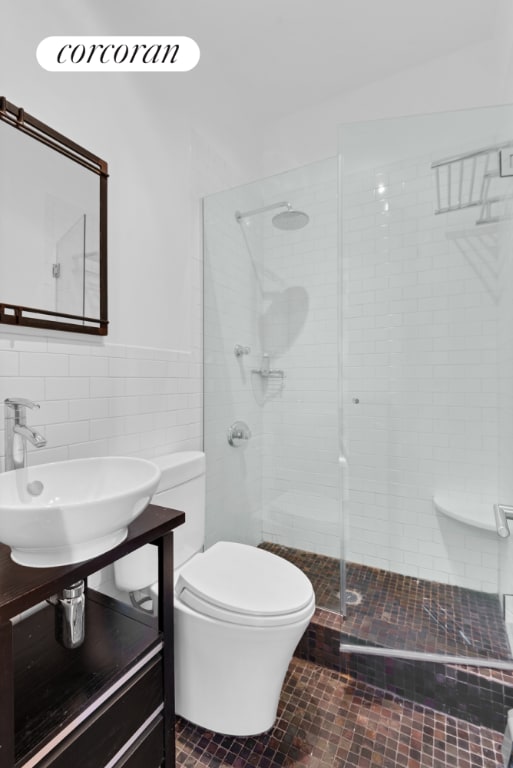 bathroom featuring tile walls, wainscoting, toilet, a tile shower, and a sink