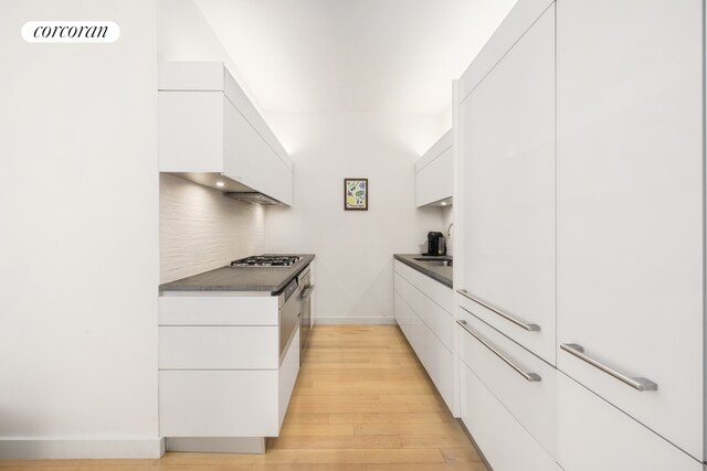 kitchen featuring stainless steel gas stovetop, white cabinets, light wood-type flooring, and decorative backsplash