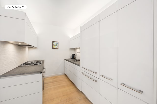 kitchen with dark countertops, stainless steel gas cooktop, white cabinetry, light wood-type flooring, and backsplash