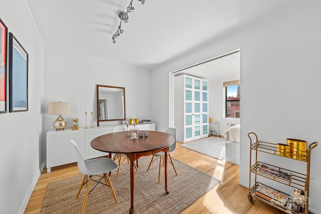 dining space with rail lighting, light wood-style floors, baseboards, and ornamental molding