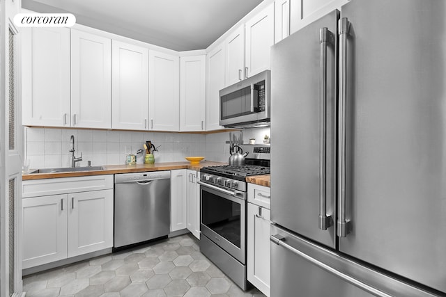 kitchen with wood counters, decorative backsplash, a sink, and stainless steel appliances