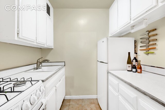 kitchen with light tile patterned floors, sink, white appliances, and white cabinets