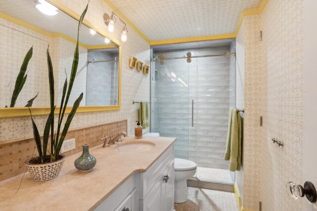 bathroom with tile patterned floors, toilet, a shower with shower door, ornamental molding, and vanity